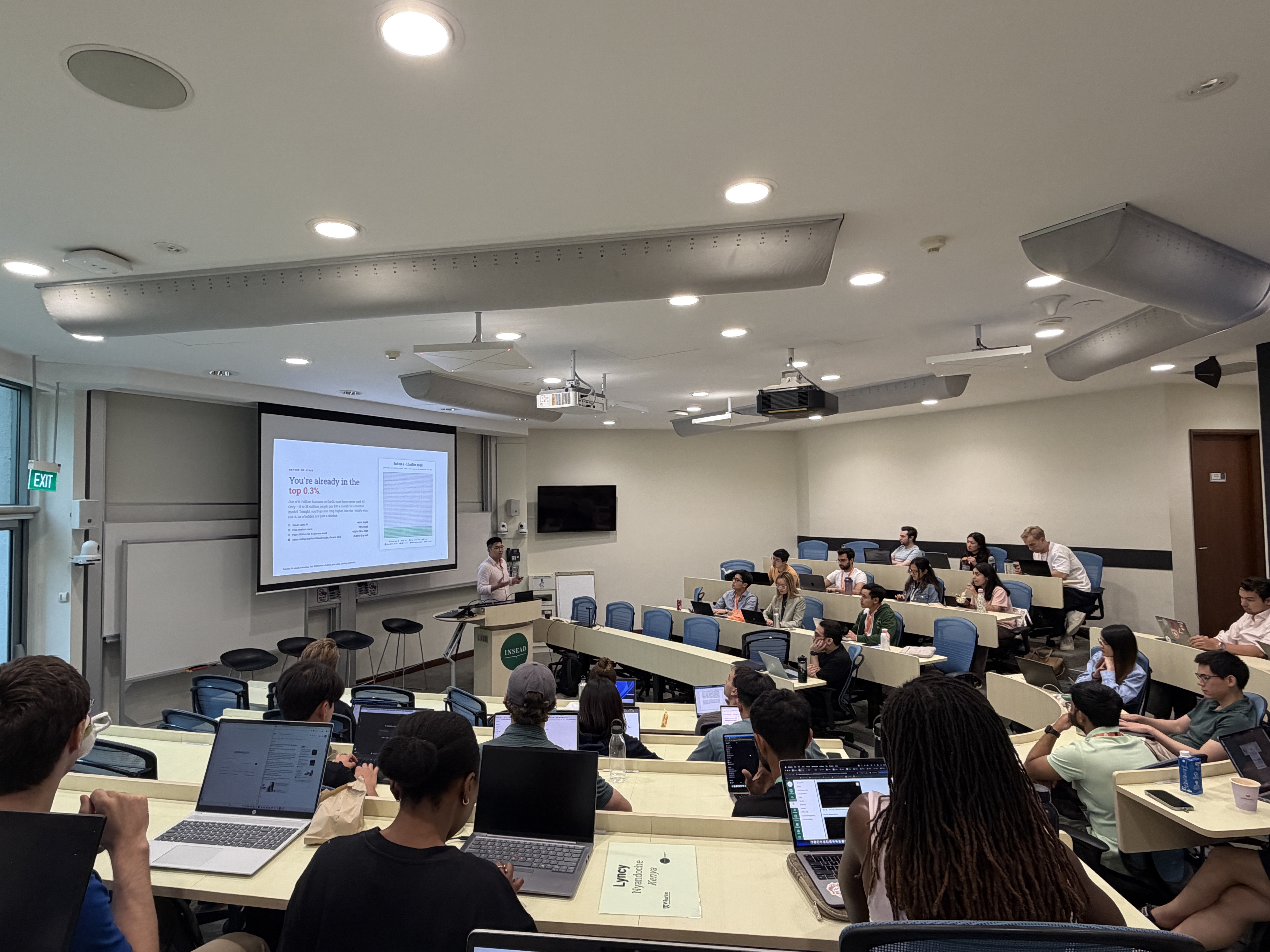 Liyang leading the Claude 101 workshop in an INSEAD lecture theatre, with classmates following along on laptops